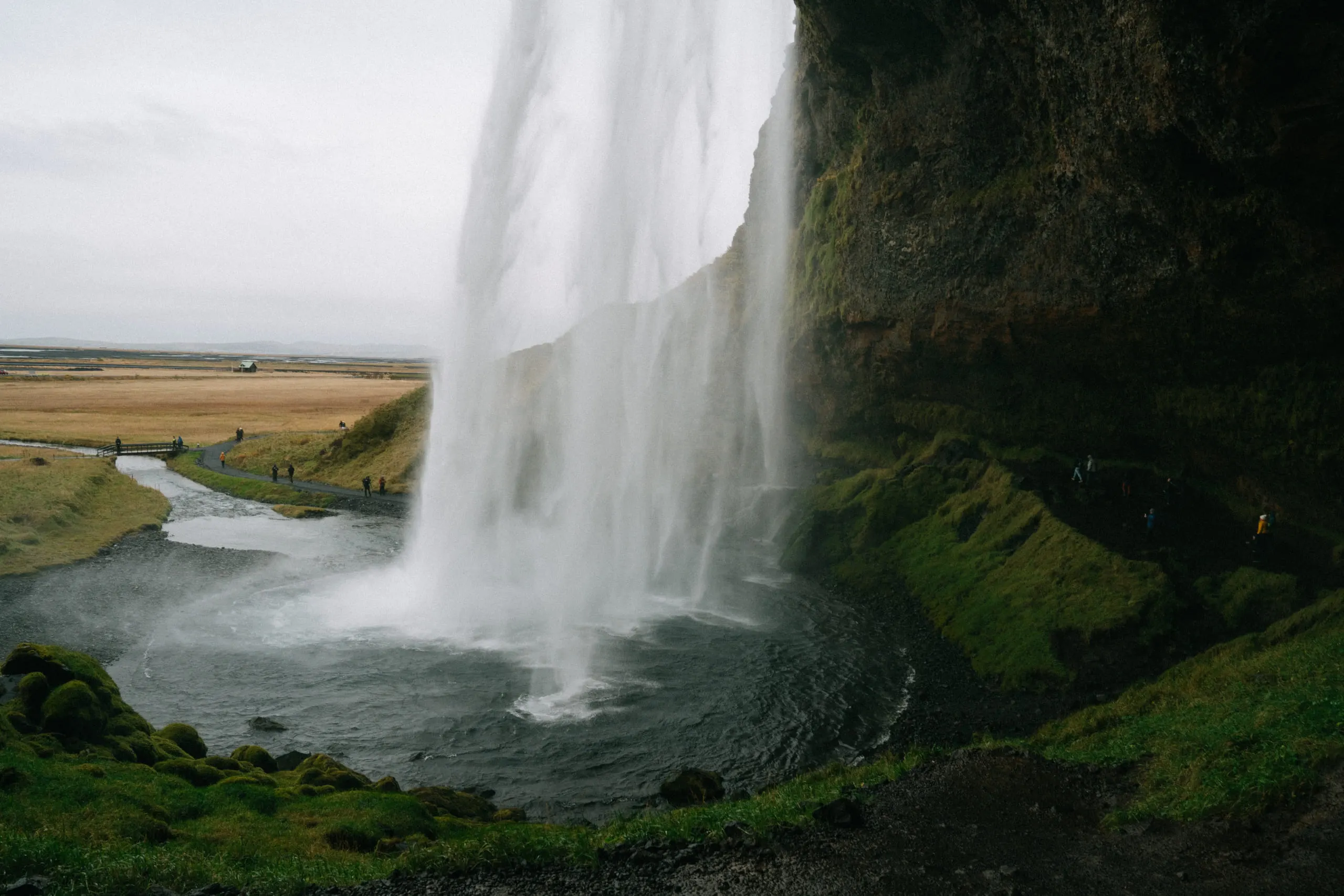 Seljalandsfoss seen from the side, water falling past the mossy overhang you can walk behind.