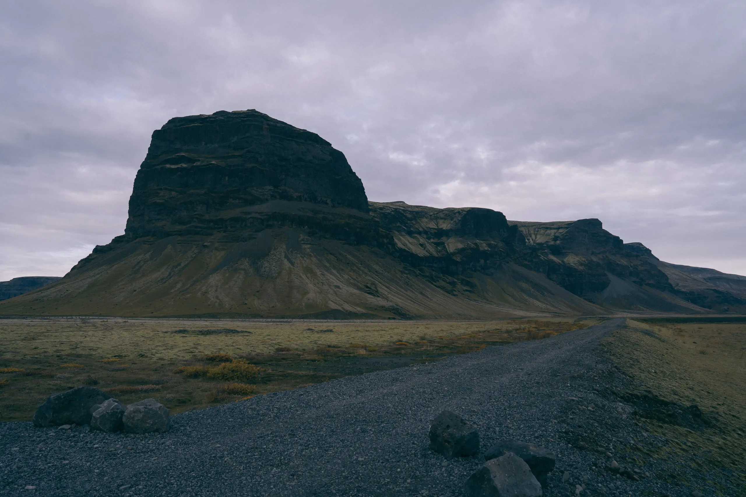 A flat-topped mountain rising abruptly from a gravel plain, a straight road running toward it.