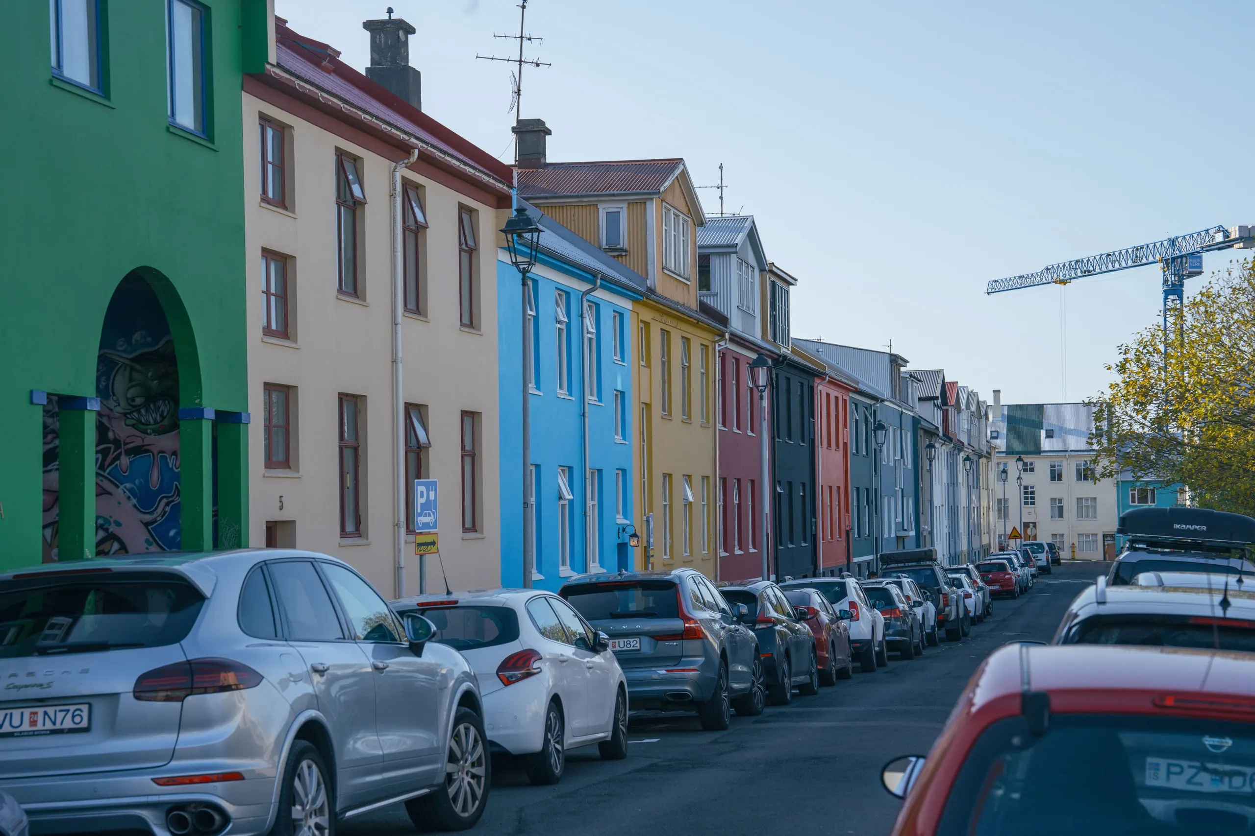 A row of brightly painted houses lining a Reykjavík street, cars parked the length of it.