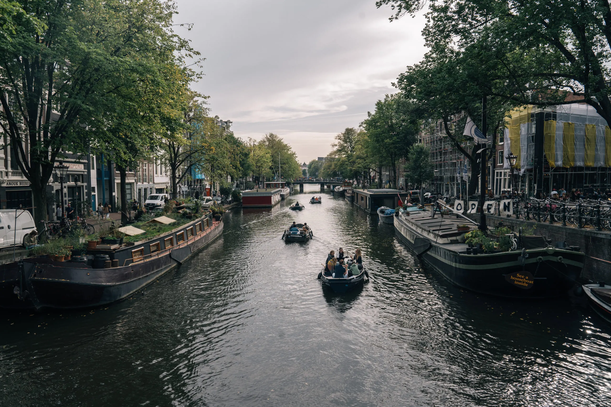 An Amsterdam canal at dusk, houseboats moored along both banks and a small boat heading up the middle.