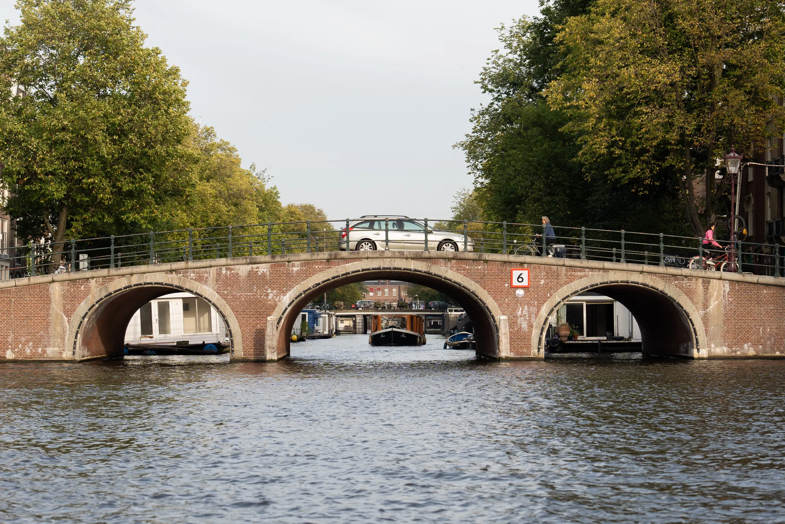 The three arches of a brick canal bridge seen at water level, further bridges receding beyond.
