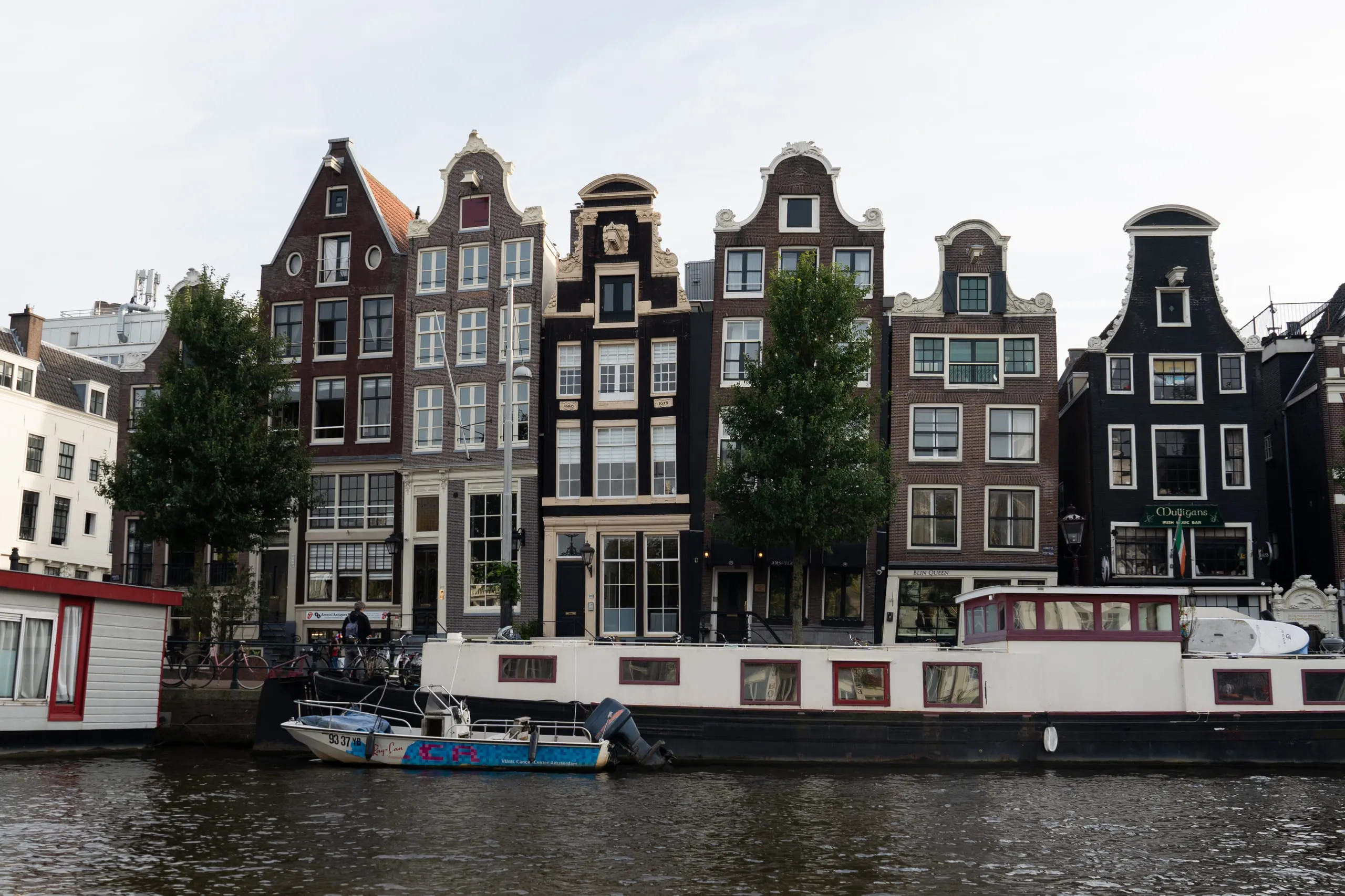 A row of narrow gabled canal houses leaning gently into one another above moored boats.