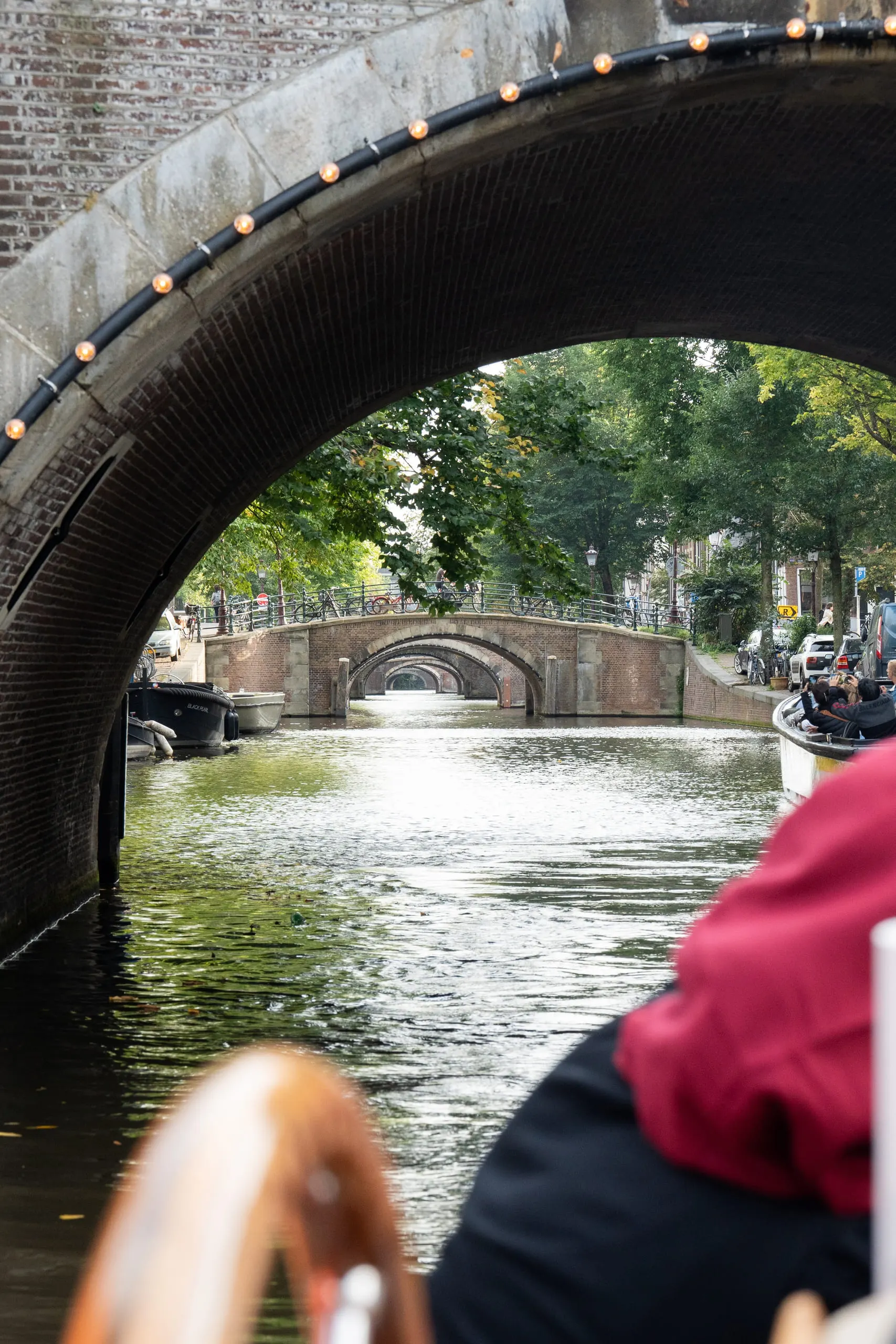 Looking up through a brick bridge arch from a passing boat, the canal opening out beyond.