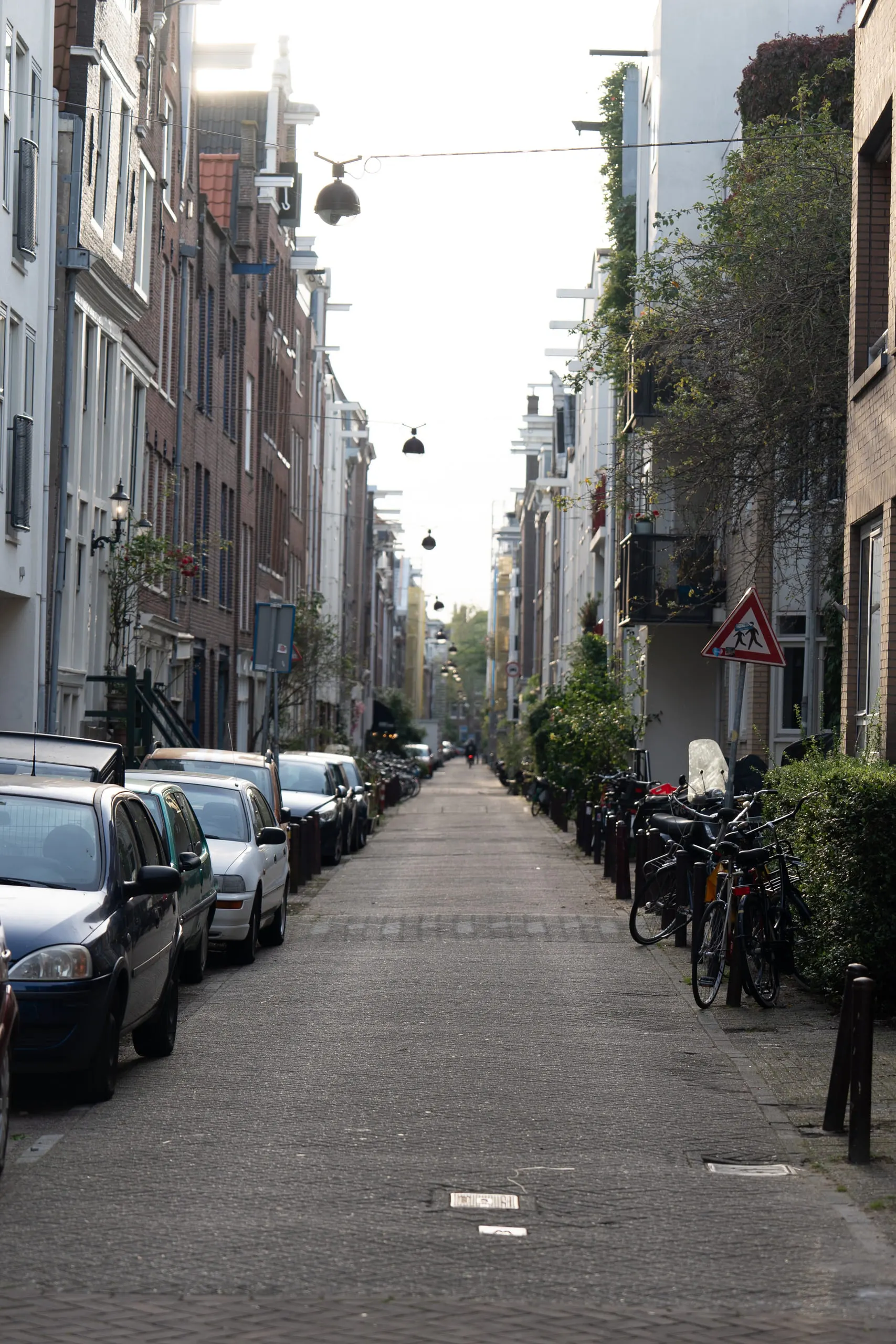 A narrow street running straight away between tall brick houses, cars and bicycles down both sides.