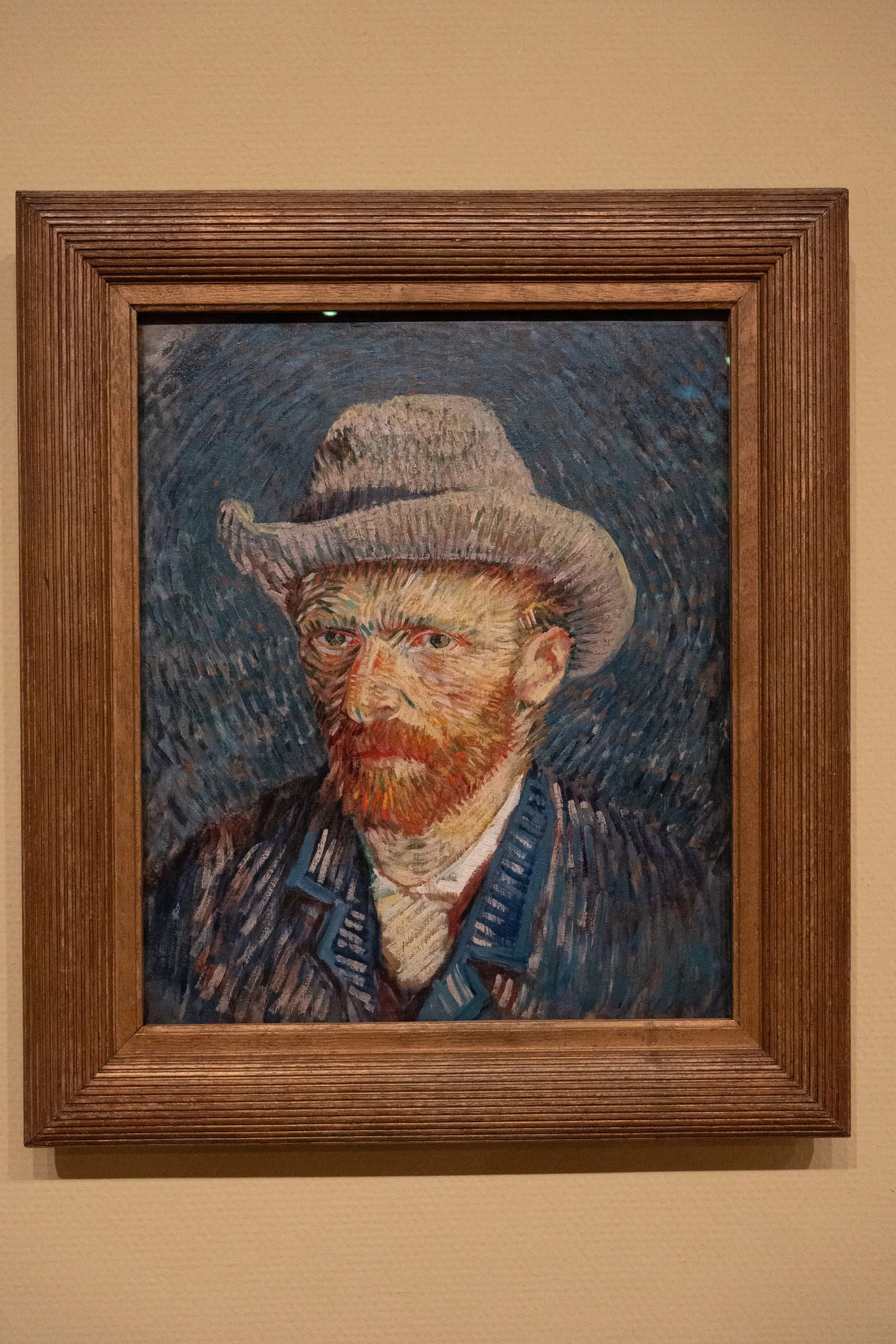 Van Gogh's self-portrait in a grey felt hat, framed on a pale wall.