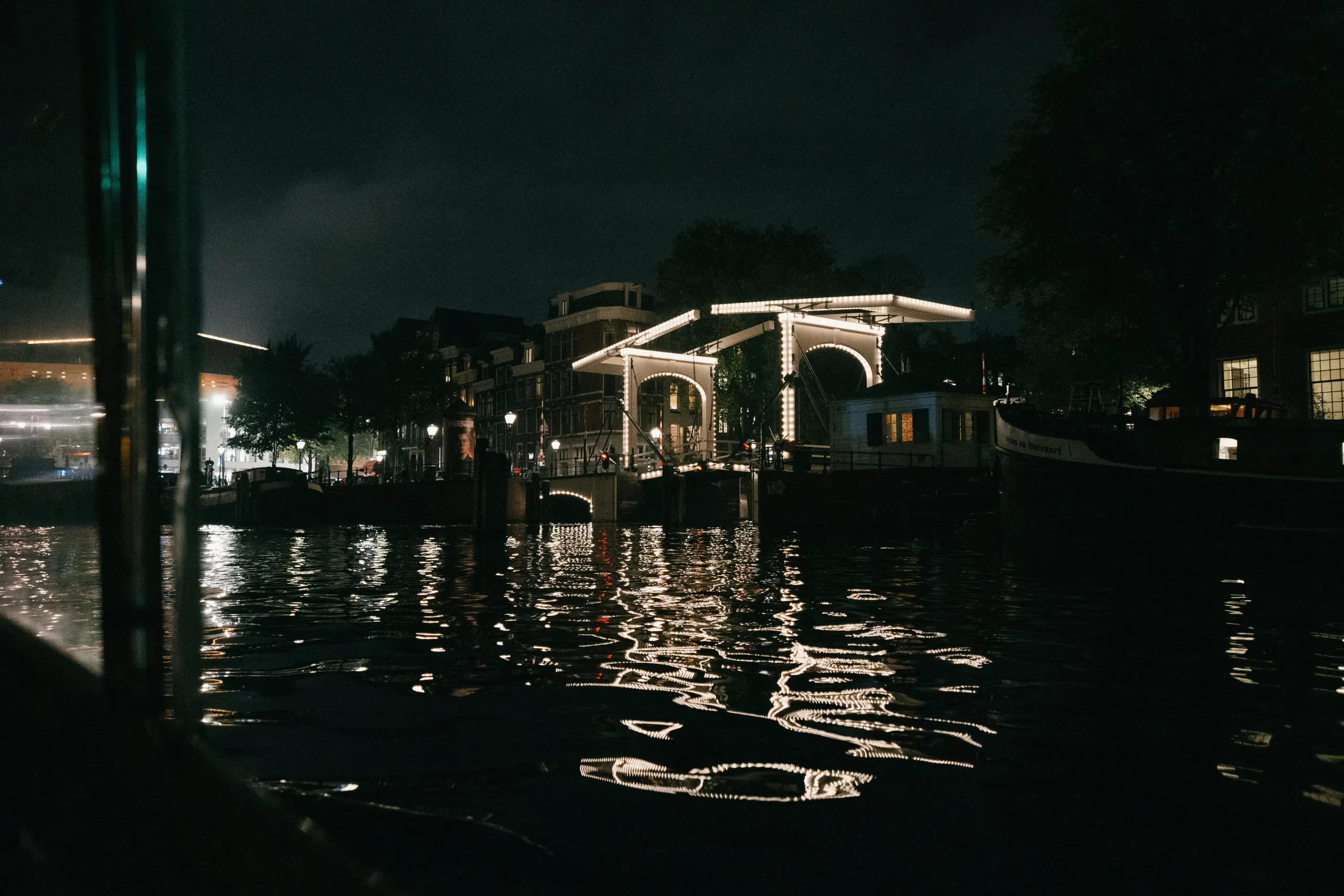 A lit drawbridge reflected in black canal water at night.