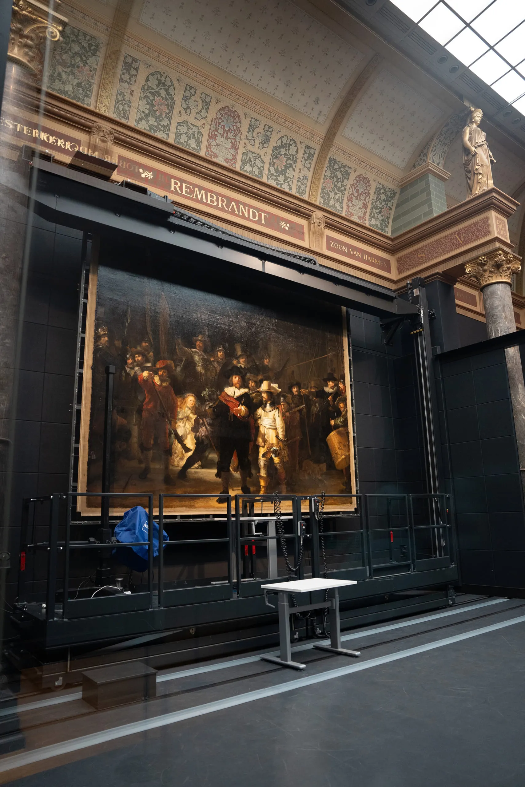 Rembrandt's The Night Watch hanging at the end of a tall gallery, viewers small in front of it.