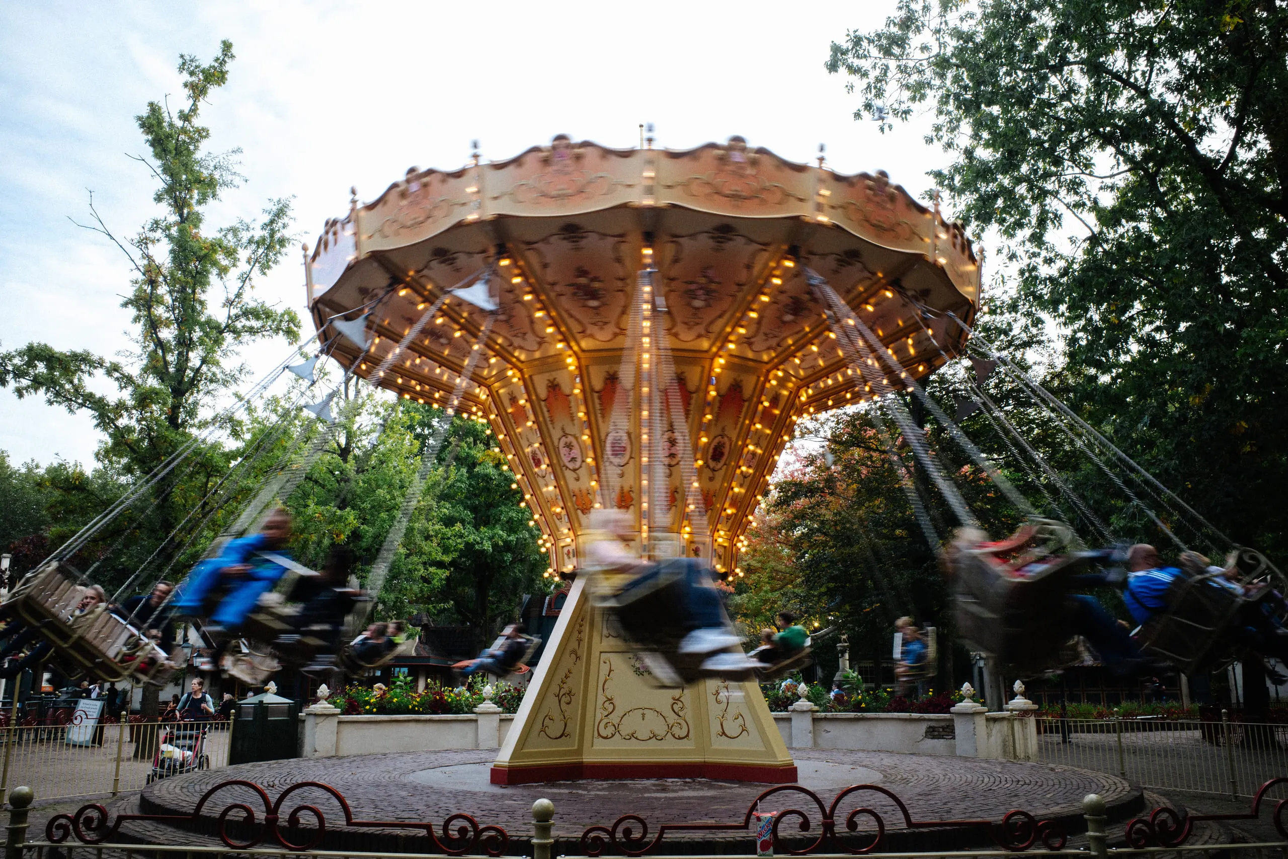 A swing carousel spinning at dusk, riders blurred into streaks beneath its lit canopy.